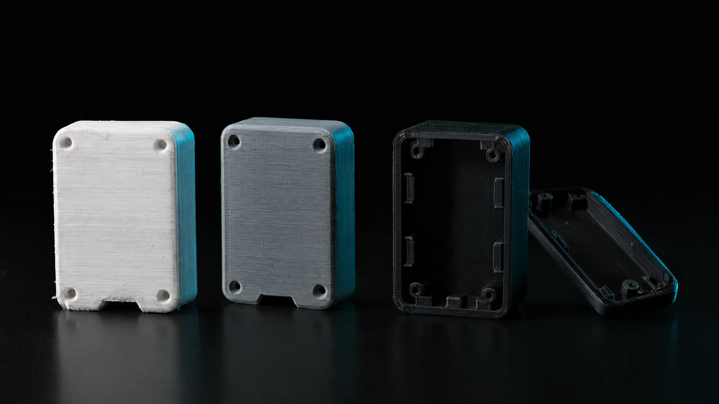Three 3D printed technical housings in white, grey and black
